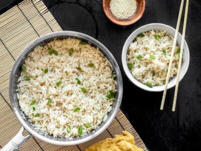 A pot full of sesame rice with a bowl of sesame rice on the side, both garnished with green onion