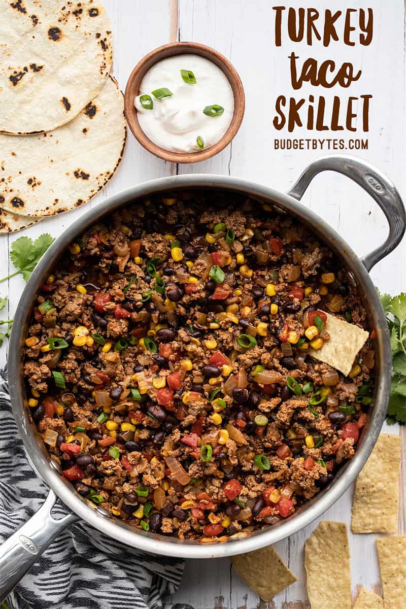 Overhead of the turkey taco skillet next to tortilla chips, toasted corn tortillas, and a bowl of sour cream. Title text at the top