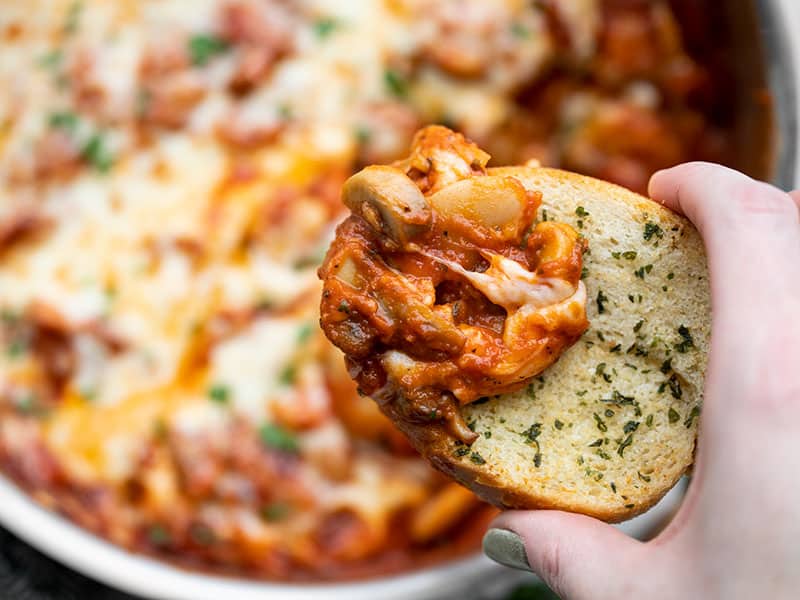 Close up of a piece of garlic bread dipped in white beans with mushrooms and marinara