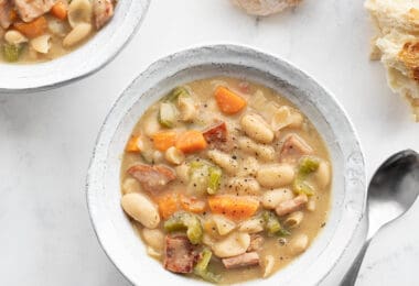 Two bowls of chunky ham and bean soup with chunks of bread on the side