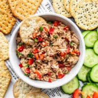 A bowl of Sesame Tuna Salad surrounded by crackers and cucumber slices