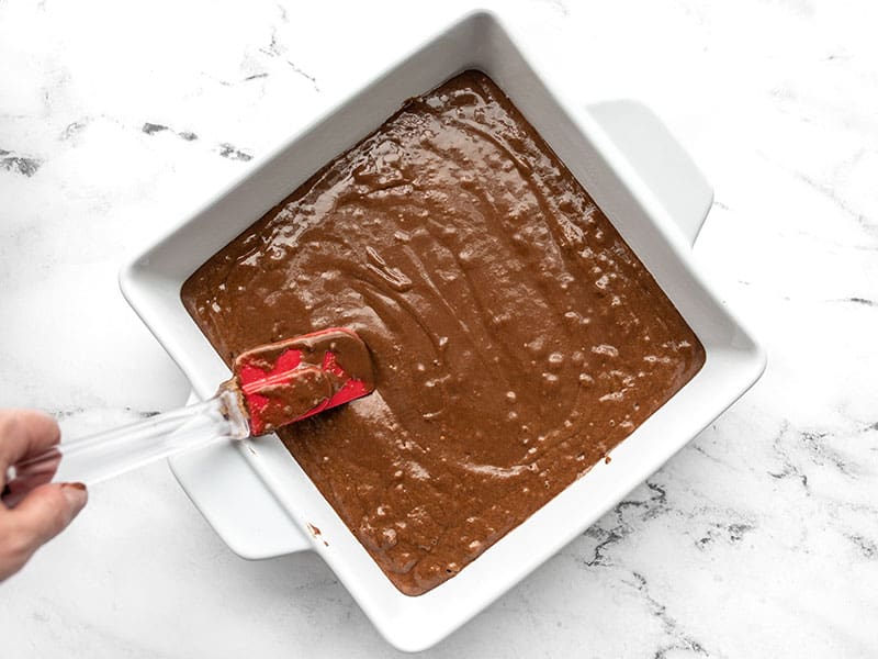 Cake batter being spread into a square baking dish