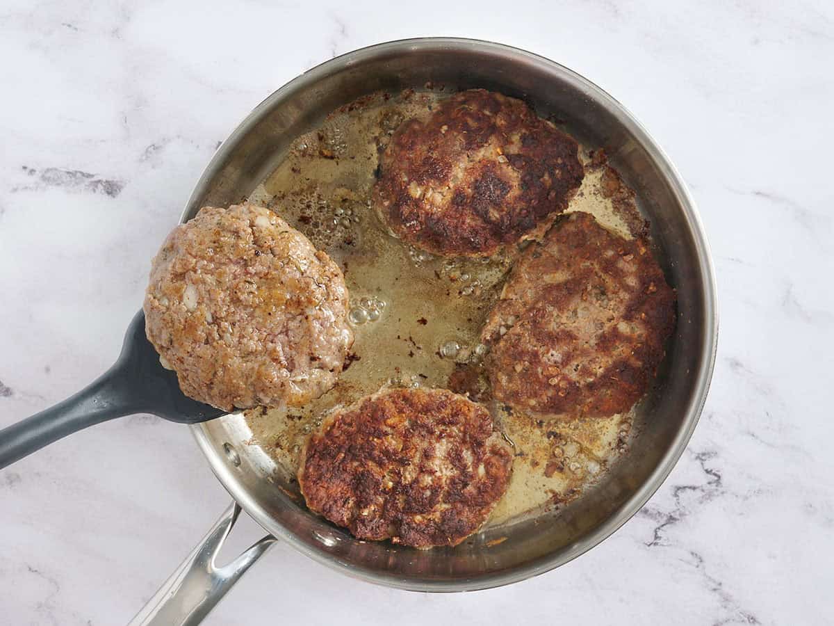 A spatula flipping Salisbury steak patties in a skillet.