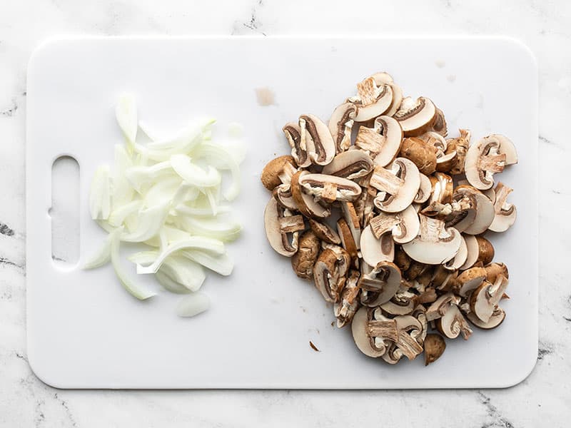 Sliced mushrooms on a cutting board with the sliced onion.