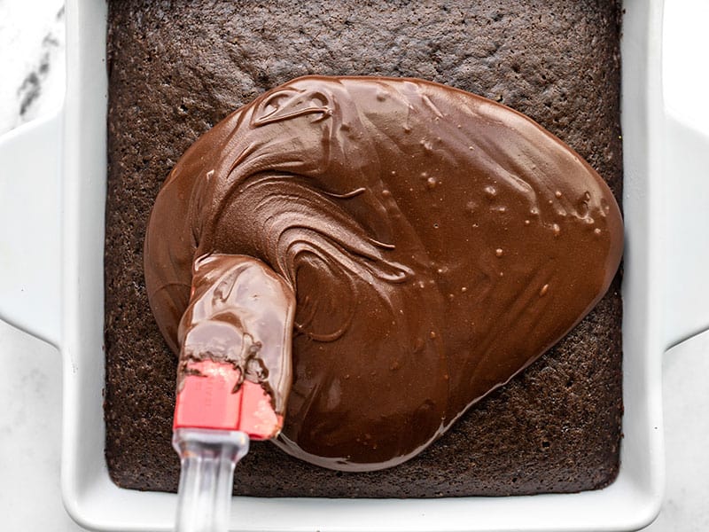 Chocolate icing being spread over the chocolate cake with a red spatula