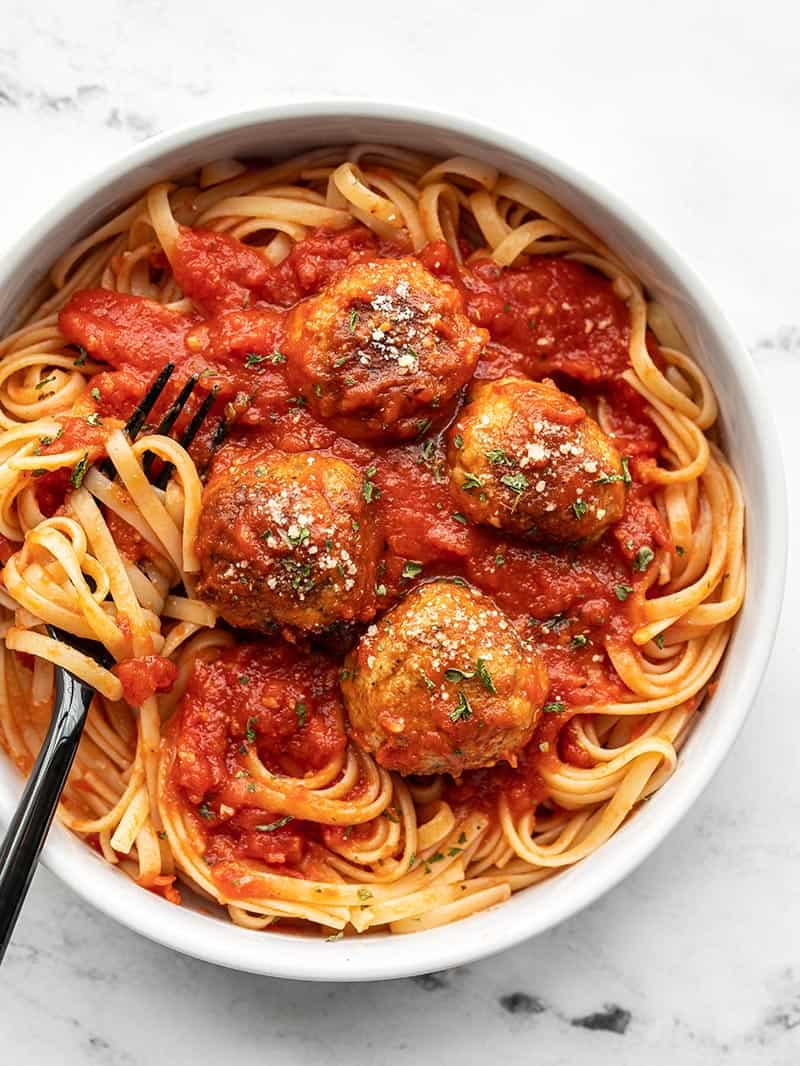 A bowl of spaghetti with sauce and chicken parmesan meatballs, a black fork twirled in the pasta on the side.