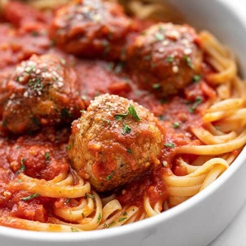 Close up side view of chicken Parmesan meatballs on a pile of spaghetti with sauce