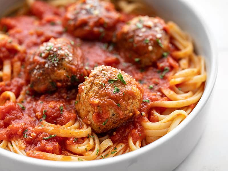 Close up side view of chicken Parmesan meatballs on a pile of spaghetti with sauce