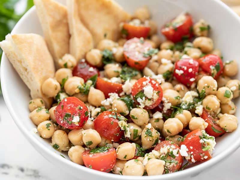 Close up side view of the bowl of Chimichurri Chickpea Salad with pita triangles in the side of the bowl