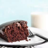 One slice of chocolate depression cake or "crazy cake" viewed from the side, a glass of milk in the background