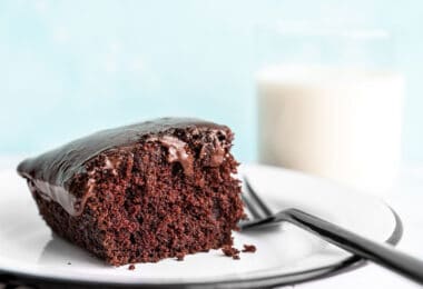 One slice of chocolate depression cake or "crazy cake" viewed from the side, a glass of milk in the background