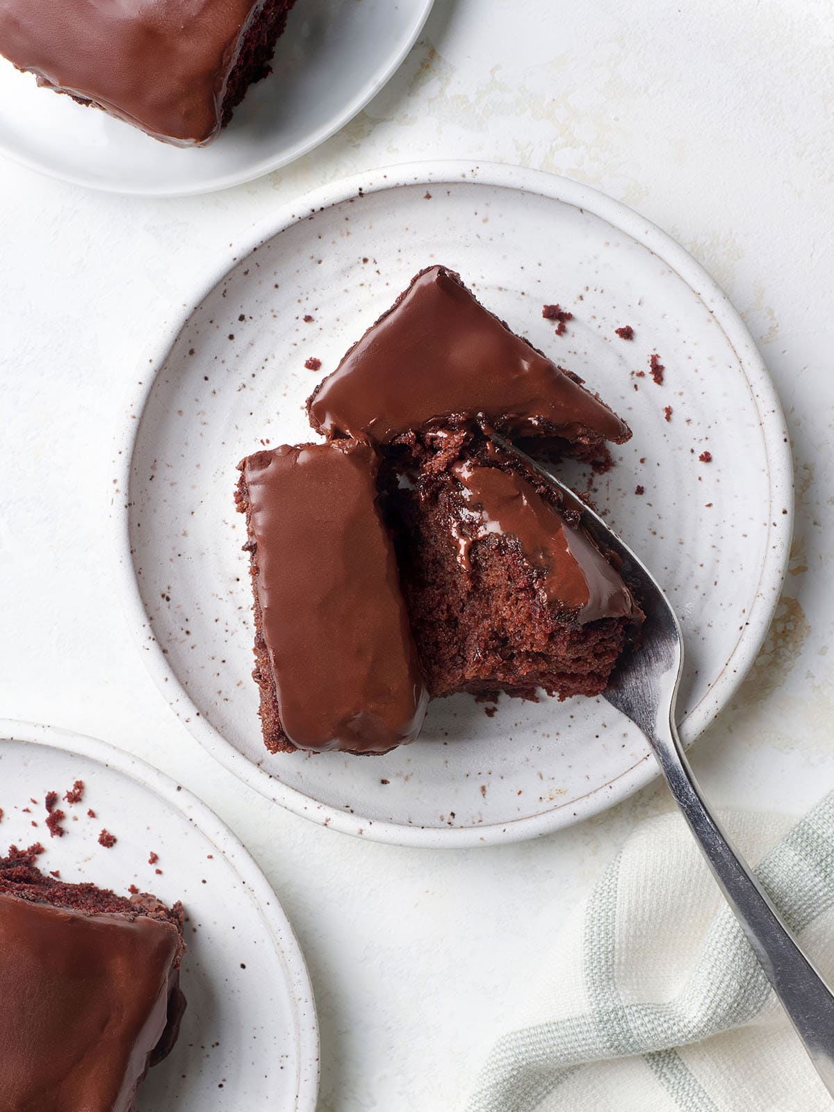 This unique Chocolate Cake recipe, popularized during the great depression, is rich and chocolatey without the using any eggs, butter, or milk! Overhead view of a slice of homemade chocolate depression cake, broken in half by a fork, on a plate.