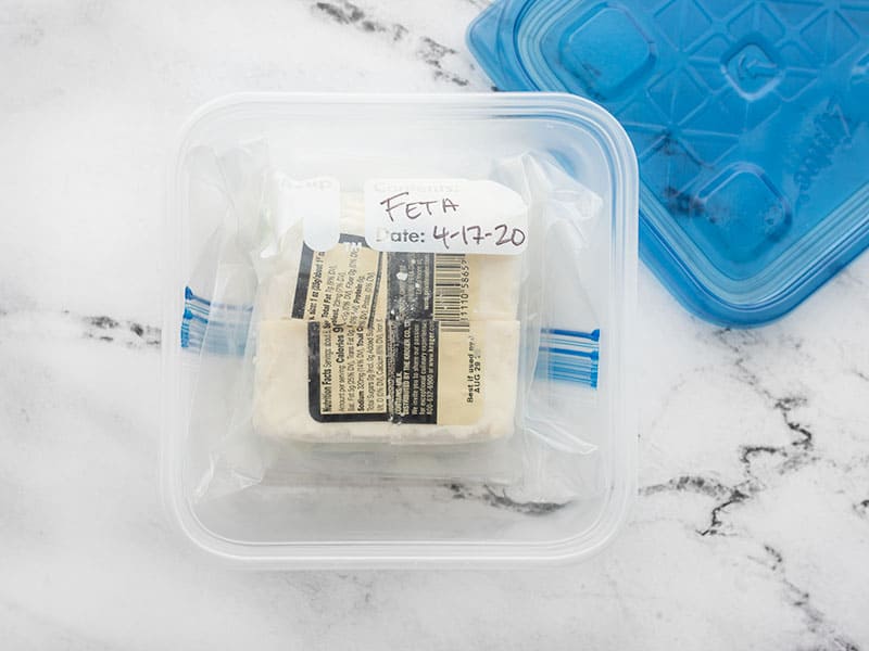 block of feta in a freezer bag, inside a plastic container, ready to freeze.