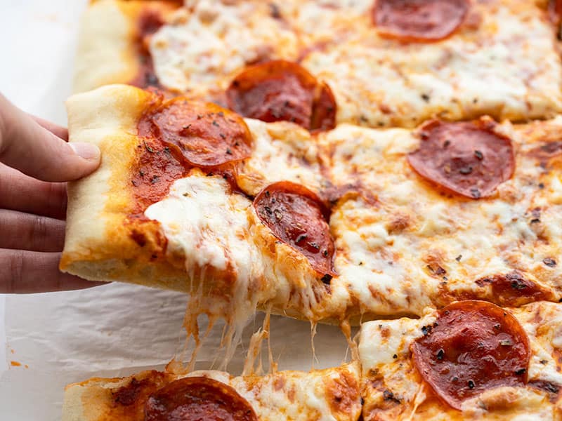 A hand lifting one slice of pepperoni pizza out of the side, with cheese pulling between slices.