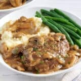 Side view of salisbury steak on a plate with mashed potatoes and green beans.