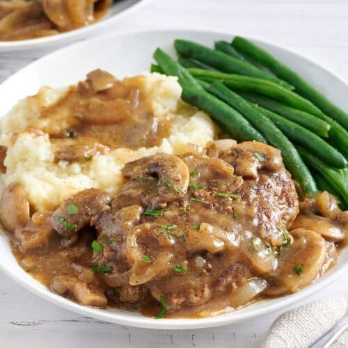 Side view of salisbury steak on a plate with mashed potatoes and green beans.