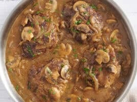 Overhead view of Salisbury steak in a skillet with mushroom gravy.