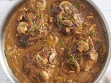 Overhead view of Salisbury steak in a skillet with mushroom gravy.