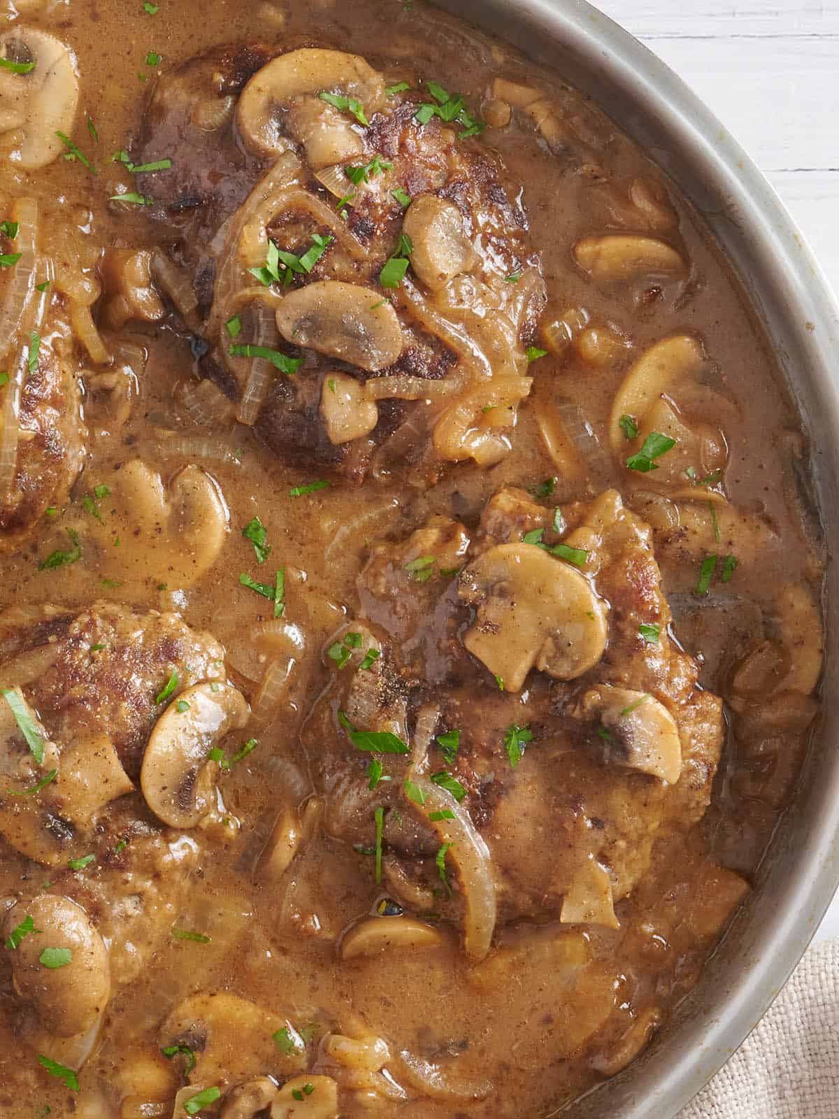 Overhead view of Salisbury steak in a skillet with mushroom gravy.