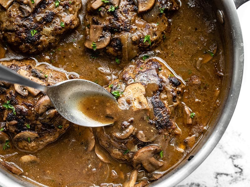 Gravy being spooned over a Salisbury Steak in the skillet