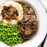 A plate full of Salisbury Steak with Mushroom Gravy, mashed potatoes, and green peas.