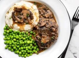 A plate full of Salisbury Steak with Mushroom Gravy, mashed potatoes, and green peas.