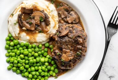 A plate full of Salisbury Steak with Mushroom Gravy, mashed potatoes, and green peas.