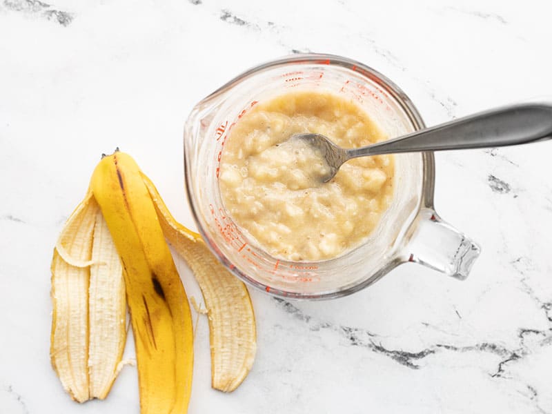 Mashed banana in a measuring cup next to a banana peel