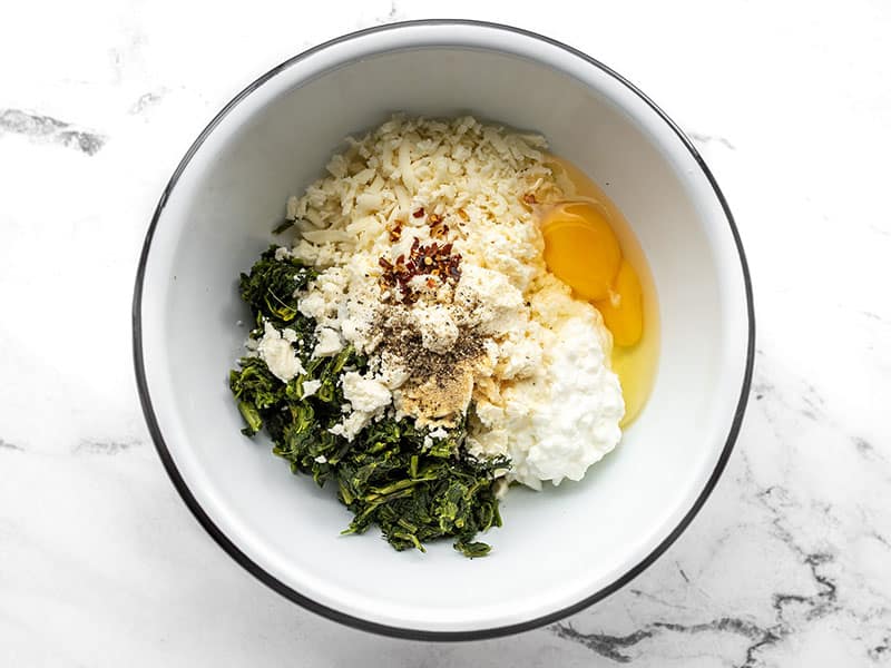 Cheese, egg, and spices added to spinach in the bowl