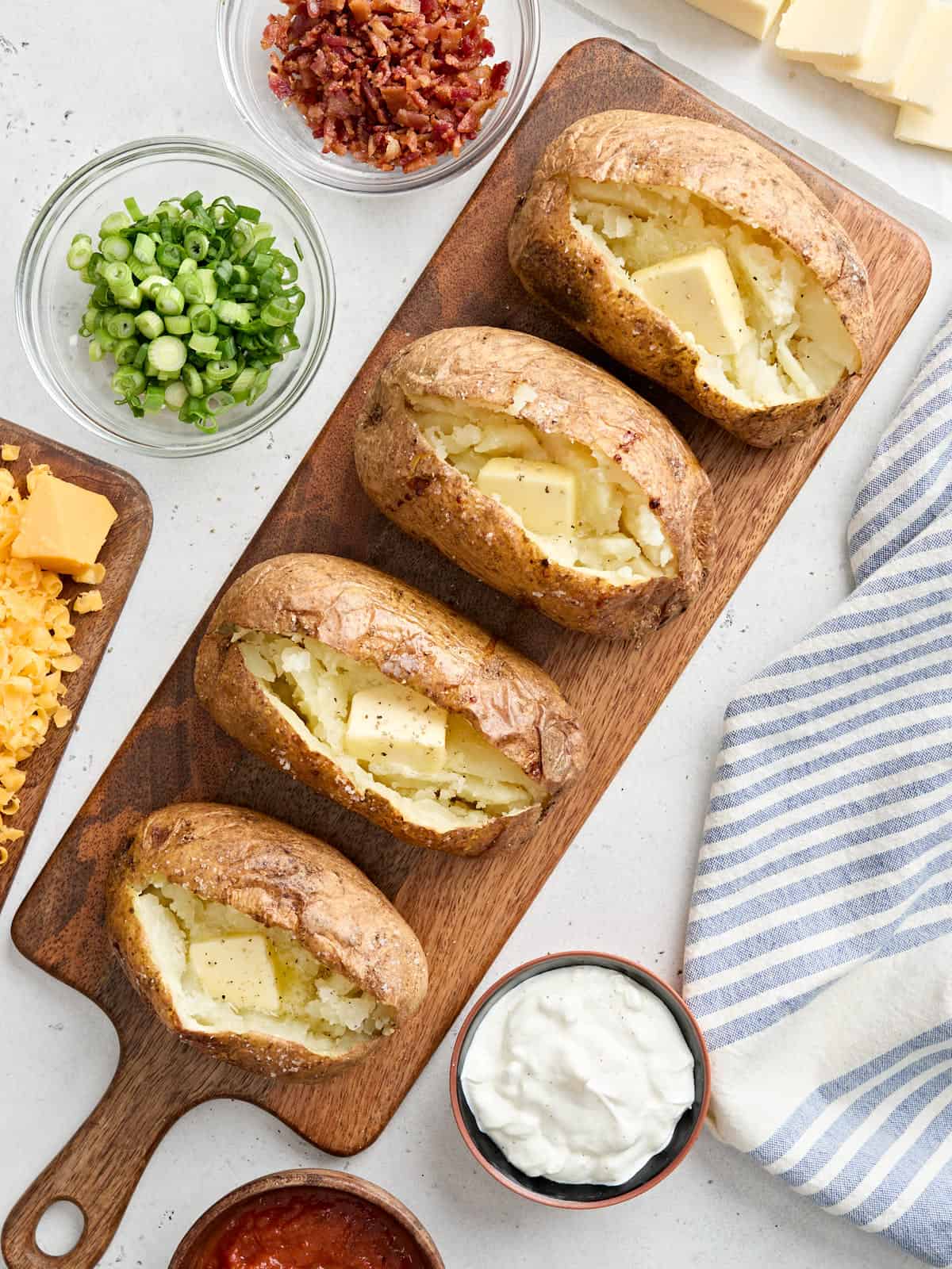How to make baked potatoes with flavorful, crispy skin and fluffy insides in three easy steps. Plus baked potato topping ideas to make it a meal! Budetbytes.com Overhead view of four homemade baked potatoes on a wooden board, topped with butter.