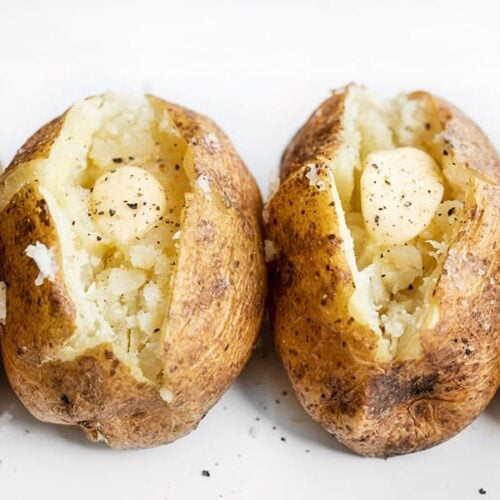 Side view of baked potatoes lined up, seasoned with pepper and butter