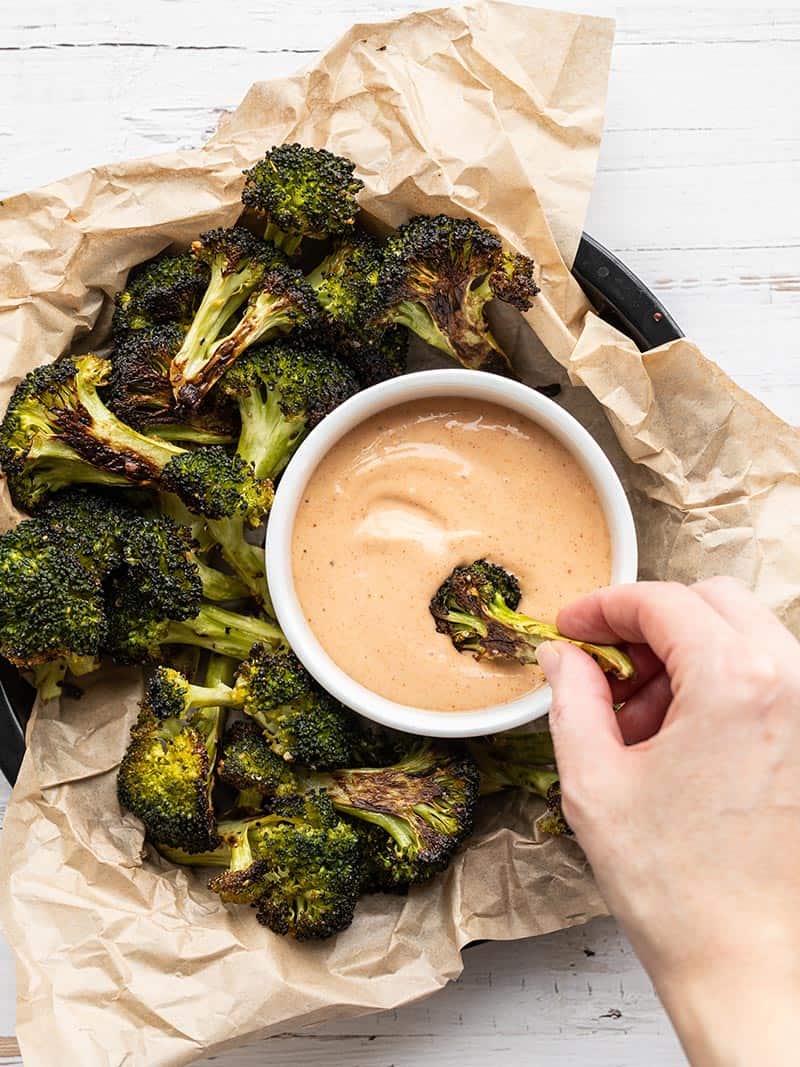 A piece of roasted broccoli being dipped into a bowl of comeback sauce
