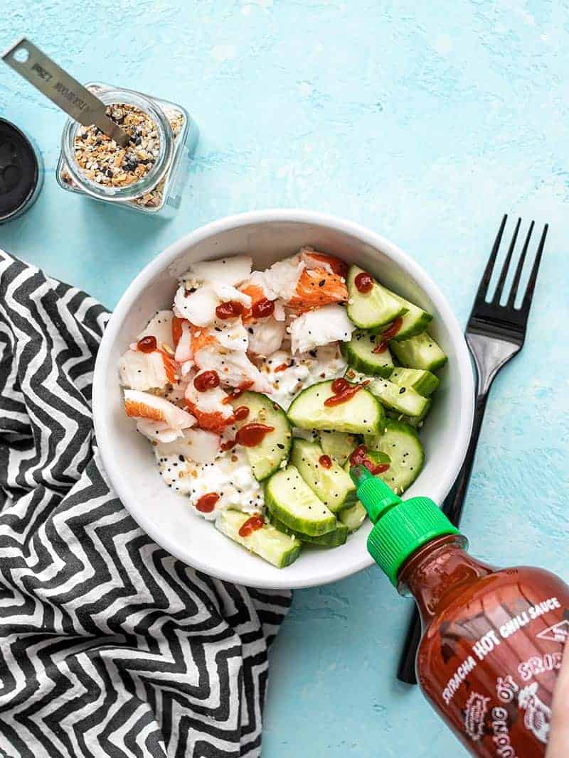 Sriracha being drizzled onto a cottage cheese crab bowl, from above