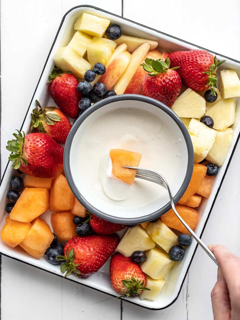 A piece of melon being dipped into the cottage cheese fruit dip with a fork