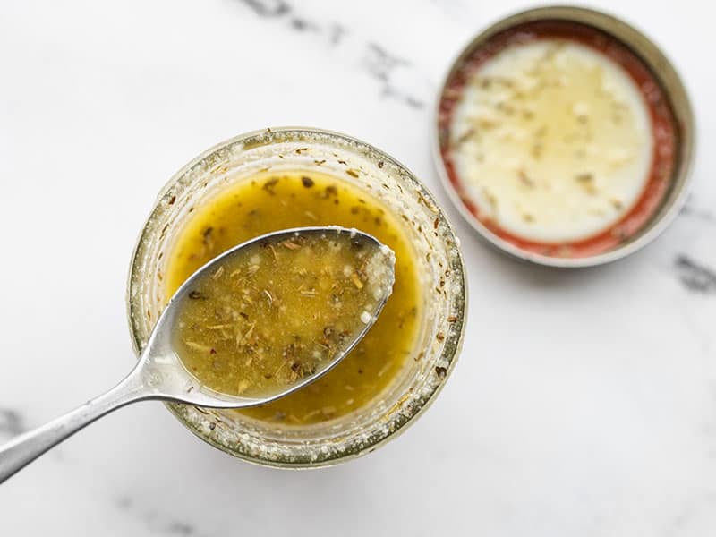 A jar of homemade Italian dressing with a spoon lifting a bit out of the jar