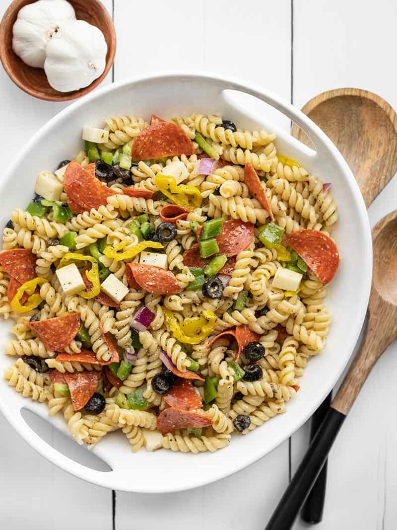 Overhead view of a serving bowl full of pizza pasta salad, wooden spoons on the side