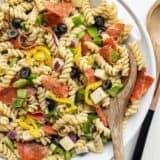 Close up of a serving bowl of pizza pasta salad, a wooden spoon in the side