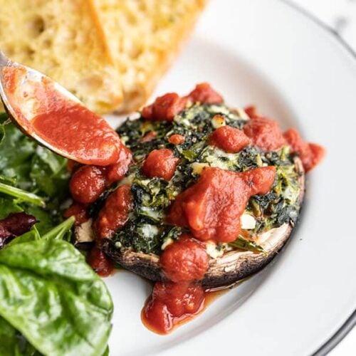 Marinara being spooned over a spinach stuffed portobello mushroom