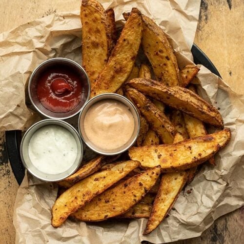 Overhead view of a plate full of steak fries with three dipping sauces