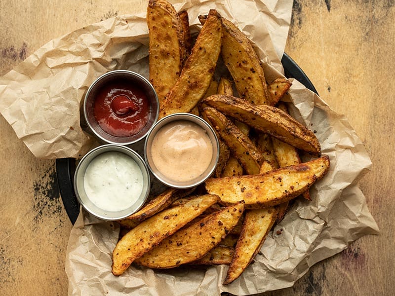 Overhead view of a plate full of steak fries with three dipping sauces