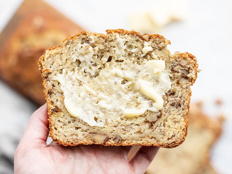 One slice of yogurt banana bread smeared with butter held close to the camera