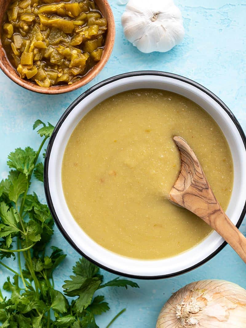 A bowl of green chile enchilada sauce with a wooden spoon next to a can of green chiles