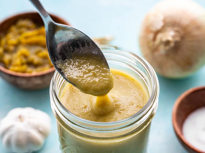 A spoon drizzling some green chile enchilada sauce into a jar of the sauce