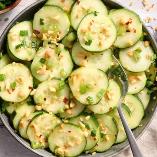 Overhead view of a bowl of sesame cucumber salad with a spoon.