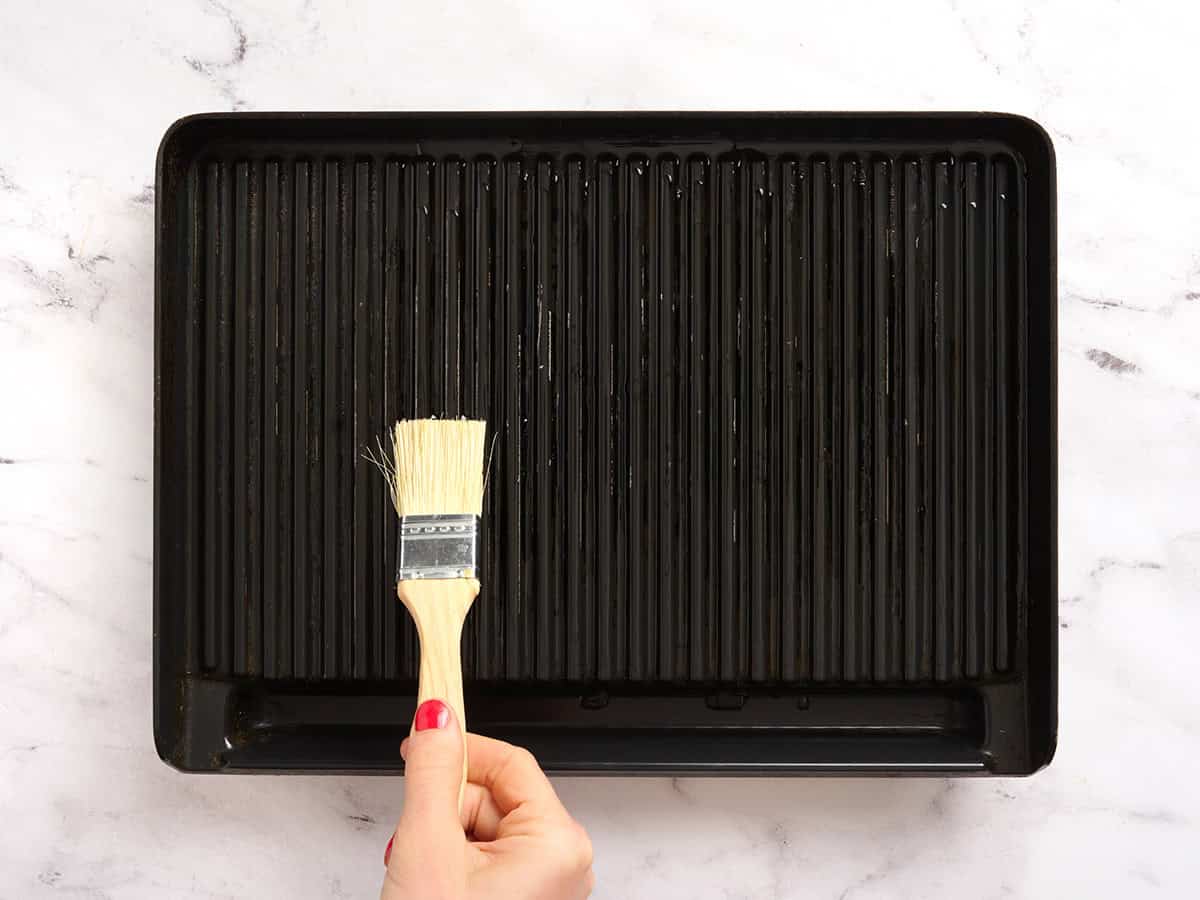 A hand brushing a grill with oil.