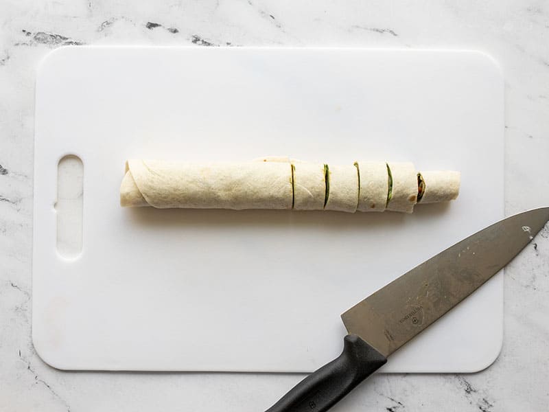 Rolled up and sliced tortilla on a cutting board with a knife