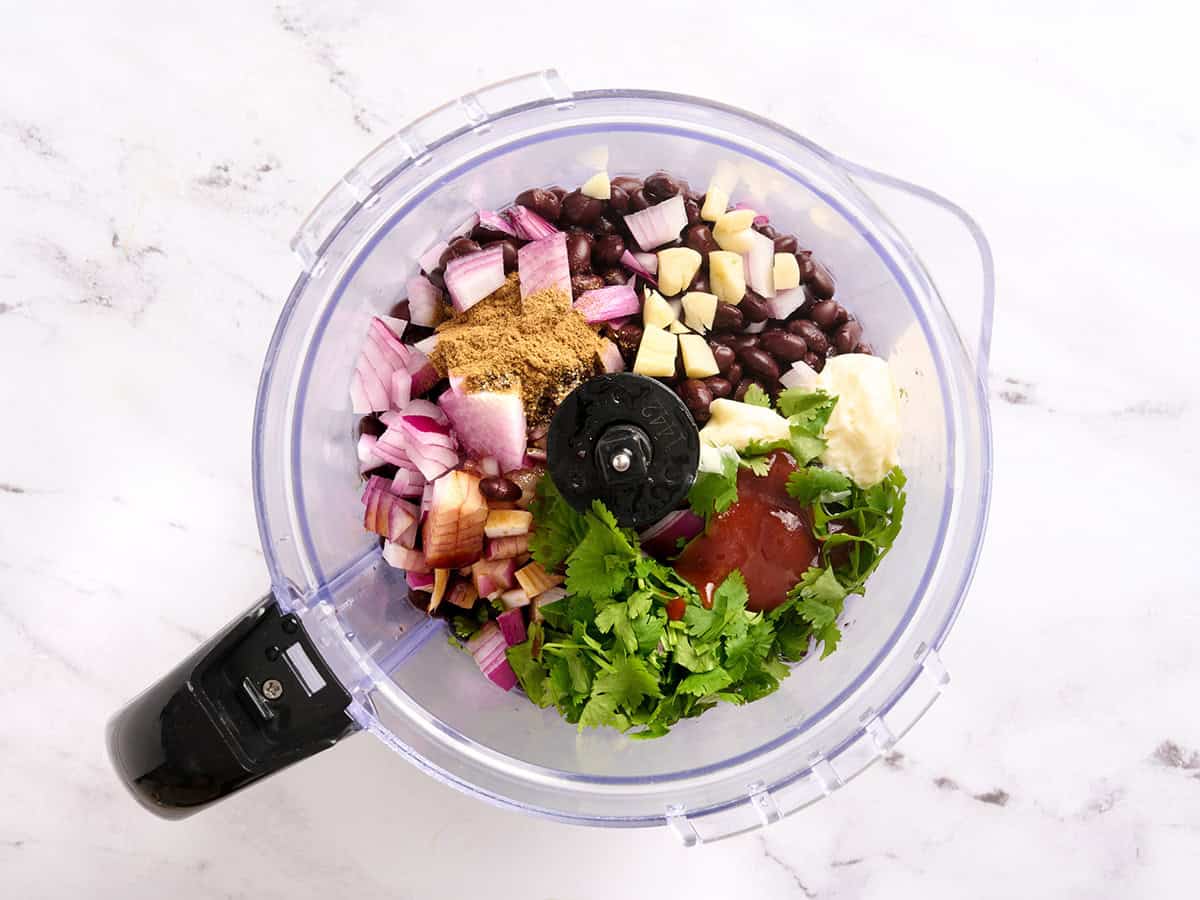 Chopped onion, sriracha, cilantro, garlic, seasonings, and black beans in a food processor.