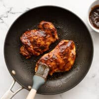 BBQ sauce being brushed onto chicken in a skillet
