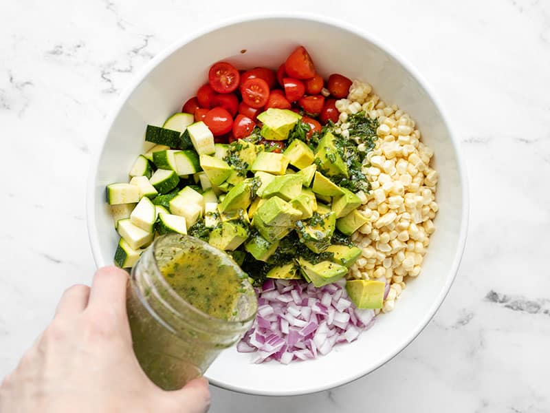 Dressing being poured over the salad ingredients in the bowl