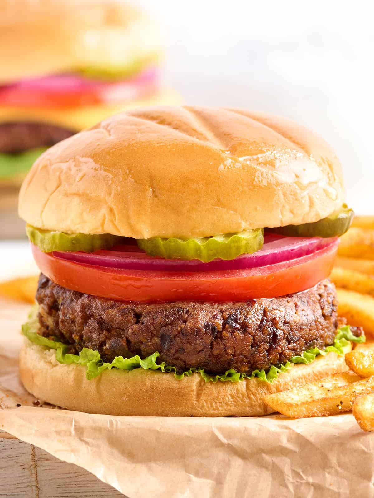 Black beans, cumin, sriracha, garlic, and fresh red onion make these homemade black bean burgers a flavorful and filling vegetarian meal. Budgetbytes.com Side view of a black bean burger in a hamburger bun with toppings.